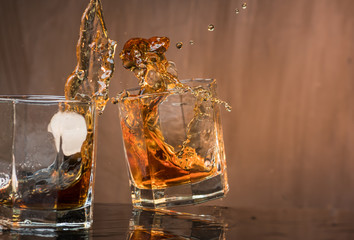 Two glasses of whiskey with ice hit and break, pouring a lot of spray and drops