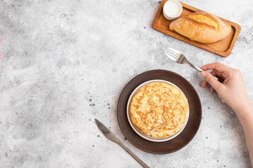 Women hand holding fork ready to start eating Spanish omelette made with eggs and potatoes and served  with mayonnaise  and bread..Top view.  .