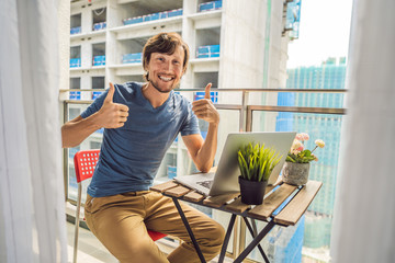 Fototapeta premium Young man trying to work on the balcony annoyed by the building works outside. Noise concept. Air pollution from building dust