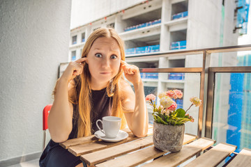 Young woman on the balcony annoyed by the building works outside. Noise concept. Air pollution from building dust