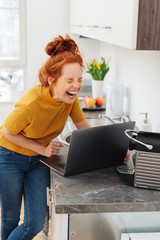 frau steht in der küche mit ihrem laptop und lacht wie verrückt