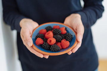 frau hält eine schale mit frischen himbeeren und brombeeren