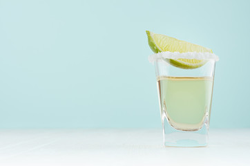 Traditional mexican alcohol drink - tequila in elegant shot glass with salt rim and green lime...