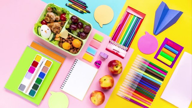 Various colorful school supplies, lunchbox and stationery on multicolor desktop timelapse, top view