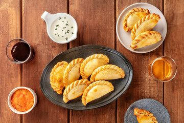 Empanadas with sauces and wine, shot from above on a dark rustic wooden background