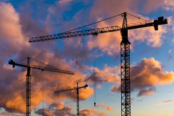 Silhouettes of construction cranes on the background of a beautiful sunset sky.
