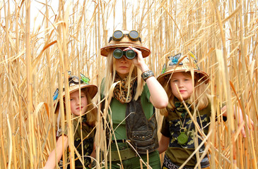 Twin young sisters and an adult girl dress up as explorers. They pose in the outdoors dressed with...