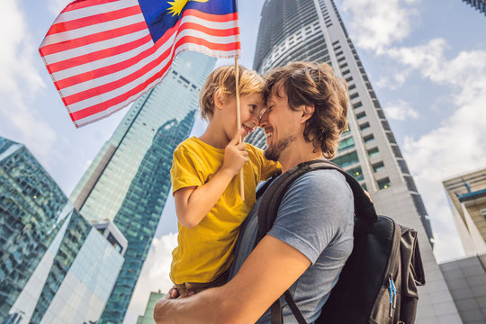 Dad And Son Tourists In Malaysia With The Flag Of Malaysia Near The Skyscrapers. Traveling With Kids Concept