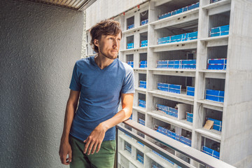 Young man on the balcony annoyed by the building works outside. Noise concept. Air pollution from...