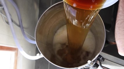 Slow motion (50fps) top shot of man pouring beer into fermenter to start the fermenting process.