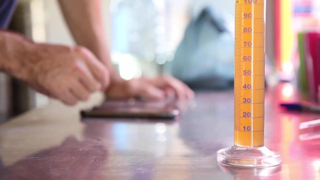 Close up shot of test tube on table with liquid inside while man does calculations in the background