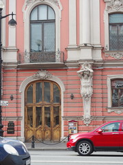 Facade of old building on Nevsky Avenue with cars riding along, Saint-Petersburg, Russia. Atlas statue holding a pilaster.