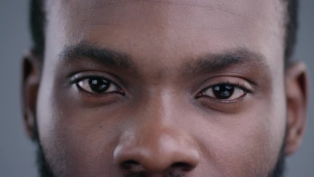 Close-up view of afro-american man eyes blinking and looking straight. Detailed portrait of confident and calm black guy staring at camera.
