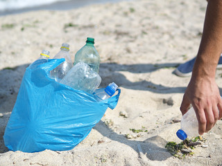 Man picking bottles into garbigde bag. Cleaning the beach in the morning time, Volunteer concept. Plastic pollution of the environment. Cleaning the beach from trash