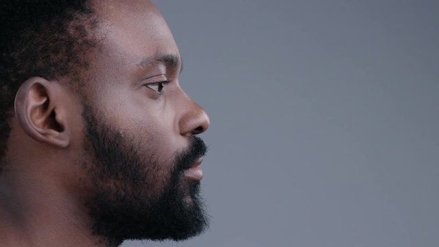 Close-up profile of handsome confident african american man with a beard looking forward isolated on grey background.