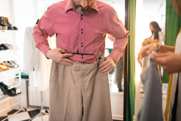 Close-up picture of adult attractive tall trying on beige trousers.