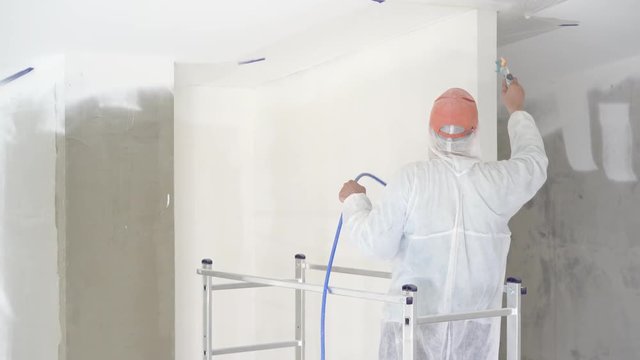 repair of the apartment - professional painter paints the walls with white paint spray gun