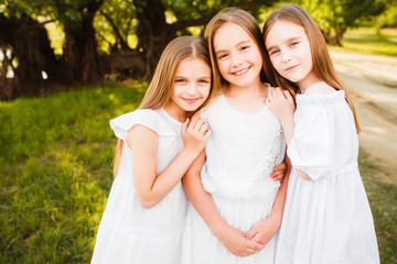 Three girls in white dresses walk in nature in the summer. Children's pastime during the summer...