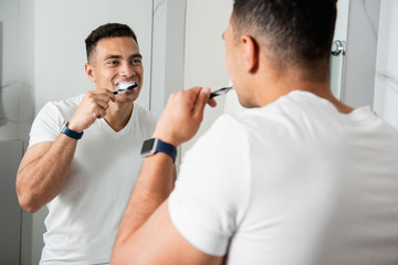 Waist up of young brunette man brushing teeth
