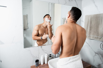 Young naked man spreading shaving foam on face