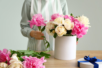 Female florist working with beautiful peonies on grey background