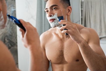 Young man shaving by razor before mirror