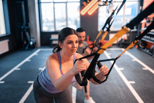 Dark-haired overweight woman feeling tired working out with TRX