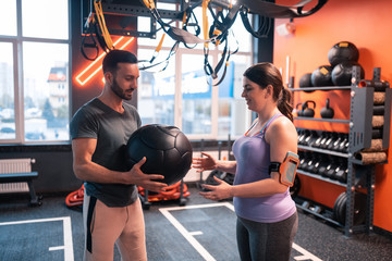 Bearded handsome trainer giving fitness ball to his client