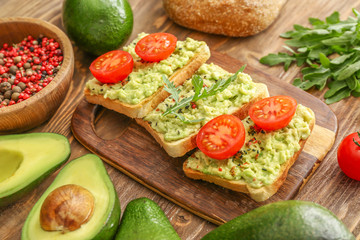 Tasty sandwiches with mashed avocado and tomato on wooden background