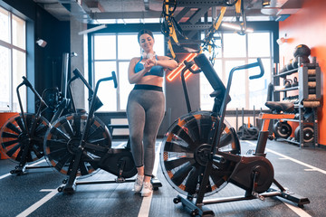 Fototapeta na wymiar Obese woman standing near exercise cycle in gym