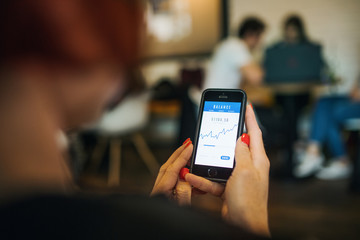 Midsection of woman with smartphone in a cafe, checking finances.