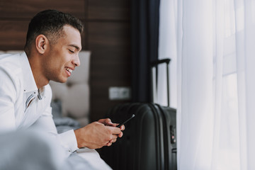 Fototapeta na wymiar Joyful man is messaging on phone indoors during business trip