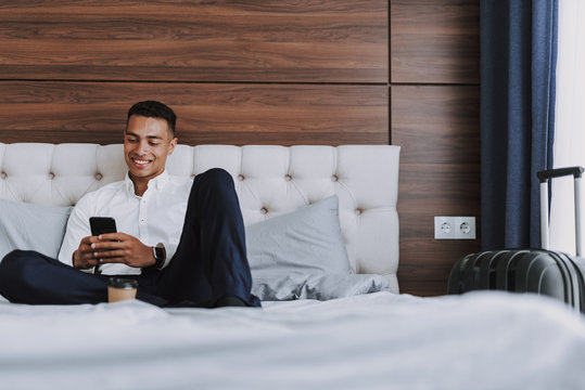Cheerful man with smartphone is drinking coffee in bedroom - Powered by Adobe