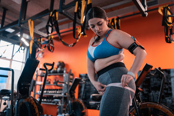 Fototapeta na wymiar Plump woman in grey leggings measuring her thighs before workout