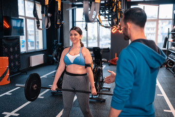Fototapeta premium Woman smiling after lifting barbell standing near trainer