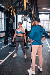 Fototapeta na wymiar Woman working on weight loss lifting barbell standing near trainer