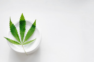 Green cannabis leaf on a jar of cream. Marijuana and hemp paste jar isolated on white. Natural...