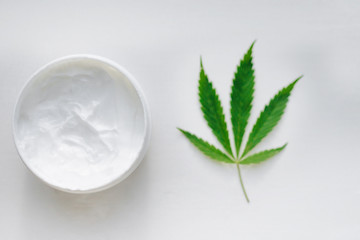 Open jar of hemp cream with cannabis leaf on white isolated background. Top view with moisturizing lotion from natural products containing CBD. Flat composition with marijuana and copy space