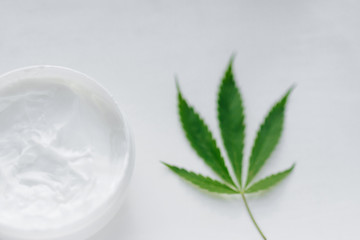 Open jar of hemp cream with cannabis leaf on white isolated background. Top view with moisturizing lotion from natural products containing CBD. Flat composition with marijuana and copy space