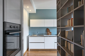 interior shot of a modern white lacquered kitchen in the foreground the steel built-in ovens the floor is made of wood