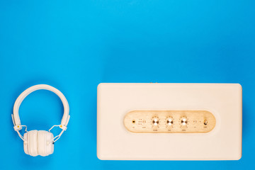 A pair of headphones next to marshall speaker on blue background, shot from above.