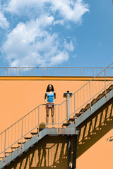 Charming young woman standing on stairs against orange wall