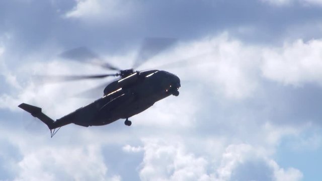 a black military helicopter (Sikorsky CH-53) flys low and sideways at an air show in Berlin. Cloudy background.