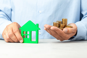 Man in blue shirt is holding a house and stack of coins. The concept of buying house, real estate...