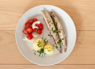 Mackerel fish dish with potatoes, chives and tomato salad. Top view of plate. Fatty, oily fish is an excellent and healthy source of DHA and EPA, which are two key types of omega-3 acid.