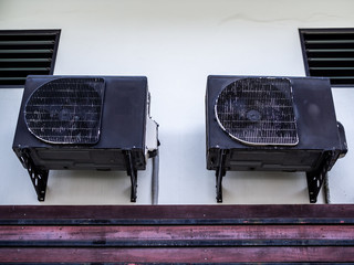 Two old black air conditioner compressors on white wall
