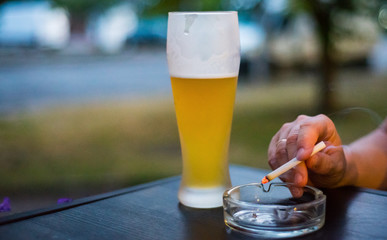glass of beer on a wooden table with ashtray and hand with smoke cigarette