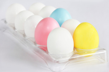 multi-colored white yellow pink blue chicken eggs in a container