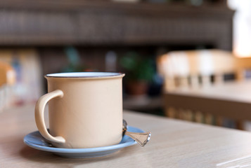 beige metal mug with a spoon on a saucer on the table in the cafe