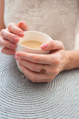  A cup of tea or coffee in the hands of a young woman. Business breakfast